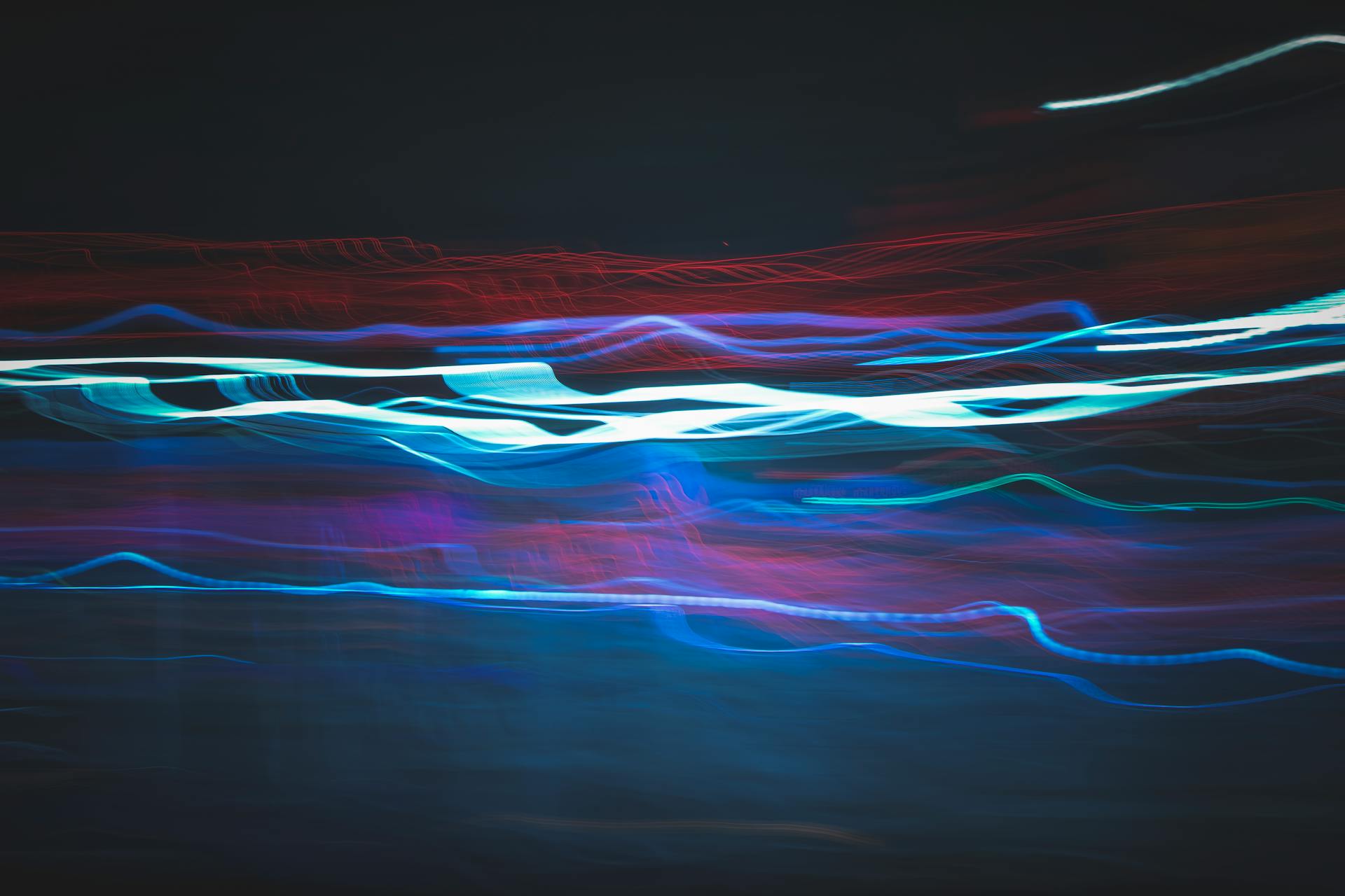 Abstract long-exposure photograph of multicoloured light trails against a dark background, featuring electric blues, reds, and purples. Featured image.